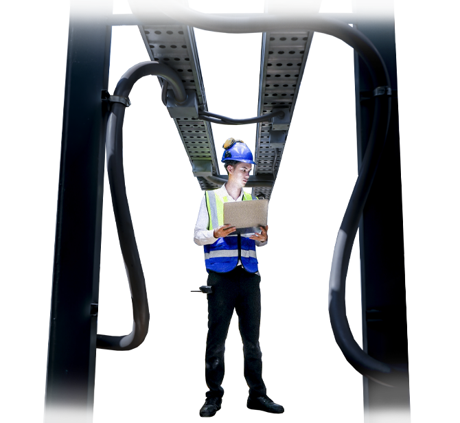 Ein Techniker mit Schutzhelm kontrolliert industrielle Anlagen und Rohrleitungen und dokumentiert seine Arbeit mit einem Tablet.