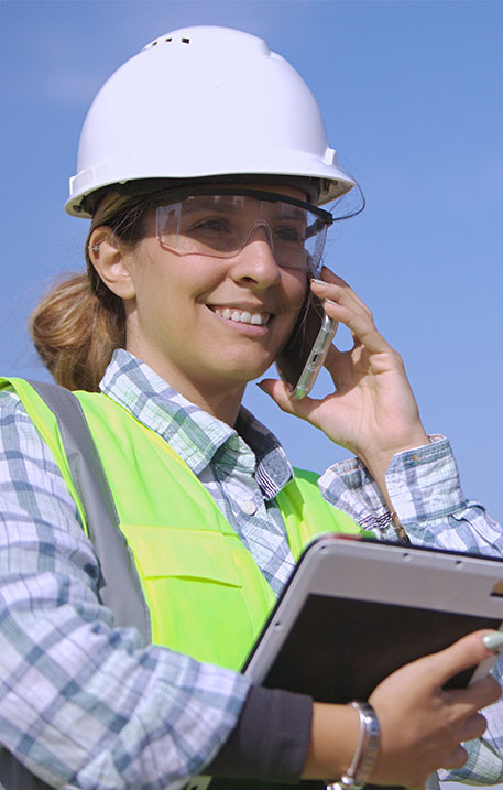 Eine Bauingenieurin mit Schutzhelm und Warnweste telefoniert auf der Baustelle und h&auml;lt ein Tablet in der Hand.