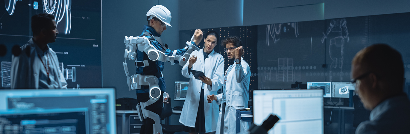 Ingenieure in wei&szlig;en Laborkitteln beobachten und analysieren einen Kollegen, der ein modernes Exoskelett im Forschungslabor tr&auml;gt.
