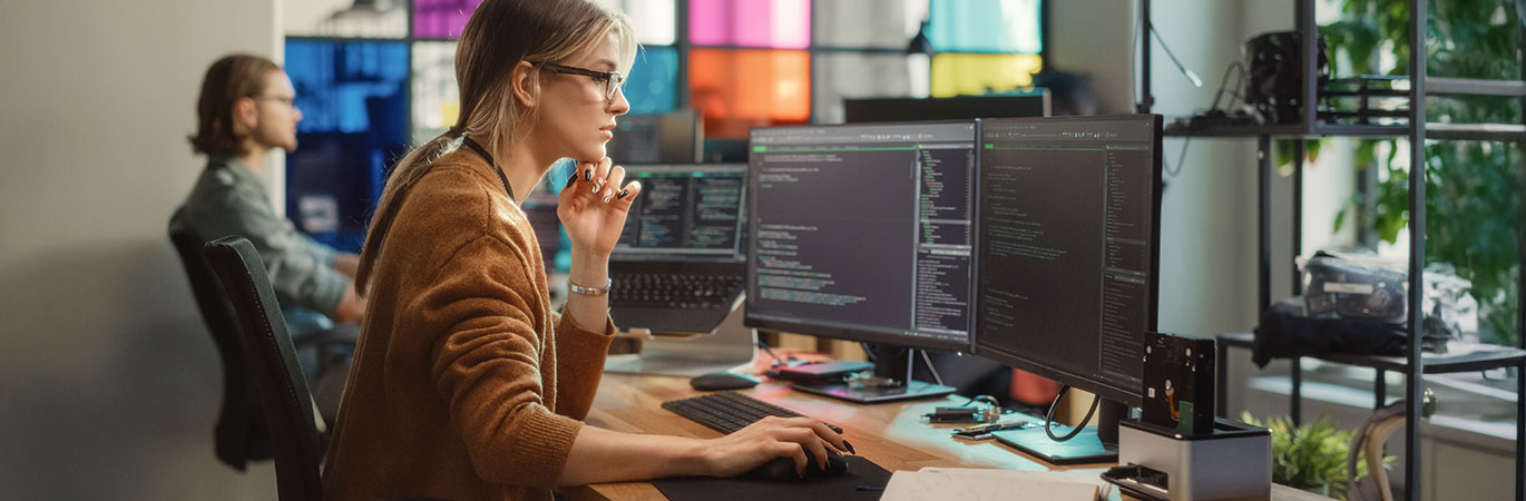 Eine Softwareingenieurin arbeitet konzentriert an zwei Monitoren mit Code in einem modernen B&uuml;ro.