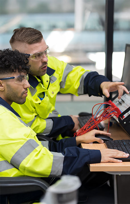 Zwei Ingenieure in Warnkleidung &uuml;berwachen mit Computern und Messger&auml;ten Tests an elektronischen Systemen.